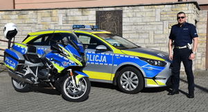 Umundurowany policjant obok oznakowanych pojazdów służbowych