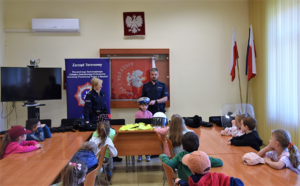 Policjanci oraz dzieci biorące udział w prelekcji. Dziecko przymierza policyjny kask