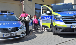 Policyjne radiowozy oraz uczniowie stojący pomiędzy nimi