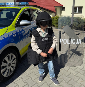 Chłopiec z elementami umundurowania stojący przed oznakowanym radiowozem