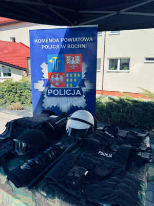 Elementy policyjnego sprzętu, umundurowanie oraz baner z logo i napisem Komenda Powiatowa Policji w Bochni