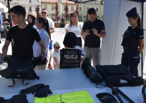 Umundurowana policjantka oraz osoby z policyjnym sprzętem i umundurowaniem