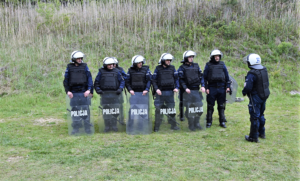 Funkcjonariusze w białych kaskach trzymający tarcze z napisem policja