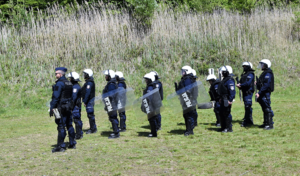 Policjanci z tarczami z napisem policja oraz bronią palną