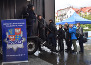 Baner i logo Komendy Powiatowej Policji w Bochni oraz osoby wchodzące do ciężarówki po schodkach